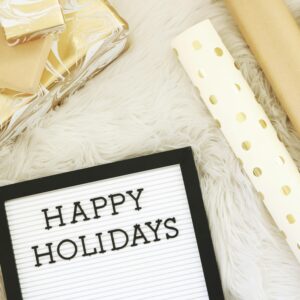 Flat lay of elegant gold and white gift wrapping essentials with a 'Happy Holidays' message board.