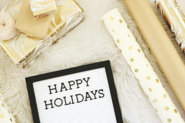 Flat lay of elegant gold and white gift wrapping essentials with a 'Happy Holidays' message board.