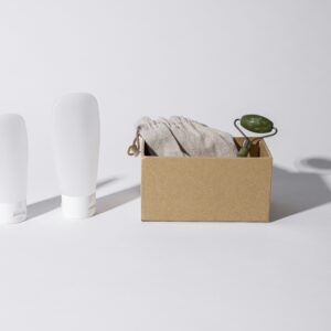 A minimalist setup of skincare essentials including a jade roller, cloth, and white bottles on a white surface.